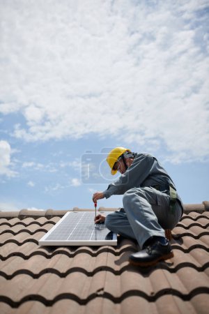 Téléchargez les photos : Constructeur en uniforme installant le panneau solaire sur le toit - en image libre de droit