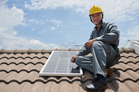 Foto de Retrato de sonriente contratista asiático instalando paneles solares en el techo de la casa - Imagen libre de derechos