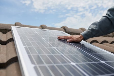 Photo for Closeup image of contractor in uniform installing solar panel on house roof - Royalty Free Image