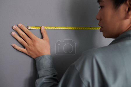 Téléchargez les photos : Constructeur en gris uniforme mur de mesure avec ruban - en image libre de droit