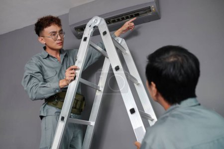 Téléchargez les photos : Travailleurs installant le climatiseur sur le mur dans la maison du client - en image libre de droit
