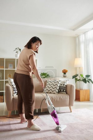 Foto de Mujer en cómoda alfombra de limpieza de vacío de ropa de casa en la sala de estar el sábado por la mañana - Imagen libre de derechos