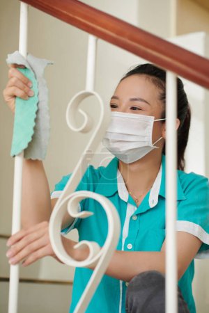 Téléchargez les photos : Nettoyant professionnel en uniforme et masque médical nettoyage garde-corps escalier dans la maison - en image libre de droit