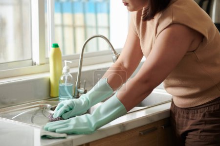 Photo for Cropped image of woman wearing silicone gloves when cleaning kitchen sink after washing dishes - Royalty Free Image