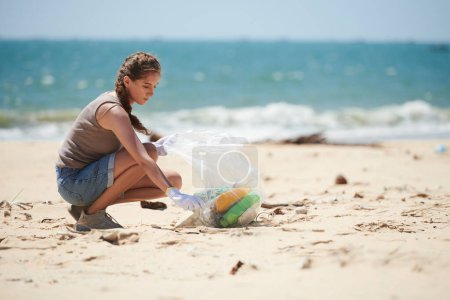 Téléchargez les photos : Jeune femme garde-côte ramassant les déchets de l'océan sur la plage - en image libre de droit
