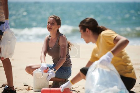 Téléchargez les photos : Jeunes positifs nettoyant les débris marins sur la plage par une journée ensoleillée - en image libre de droit