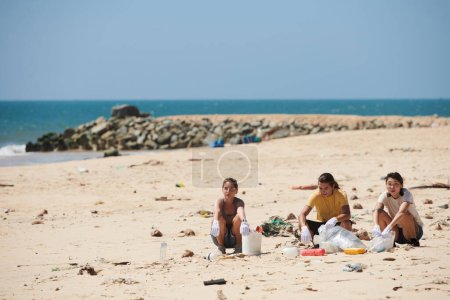 Téléchargez les photos : Groupe de jeunes gens nettoyer la plage, ramasser les déchets marins et les déchets laissés par les touristes - en image libre de droit