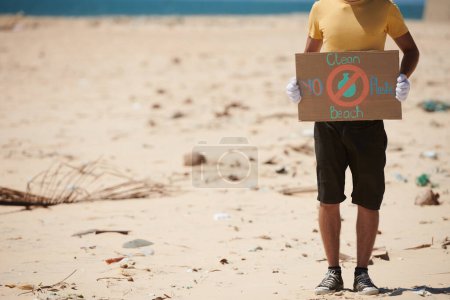 Téléchargez les photos : Image recadrée d'un volontaire tenant une pancarte de protestation sans inscription propre en plastique et sur la plage - en image libre de droit