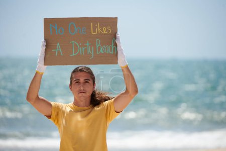 Téléchargez les photos : Jeune homme montrant personne n'aime sale pancarte de plage elle fait pour protester - en image libre de droit