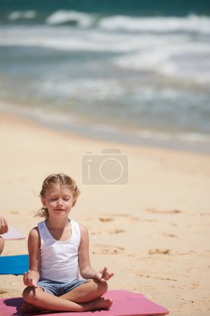 Foto de Niña sentada en posición de loto cerrando los ojos y tratando de meditar en la playa de arena - Imagen libre de derechos