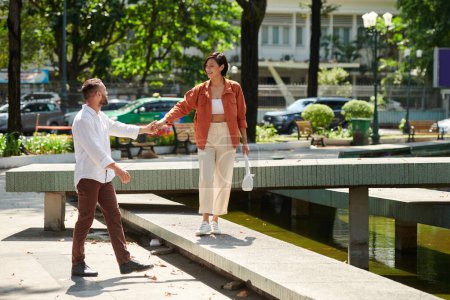 Téléchargez les photos : Homme heureux tenant la main de sa petite amie souriante quand ils marchent dans le parc - en image libre de droit