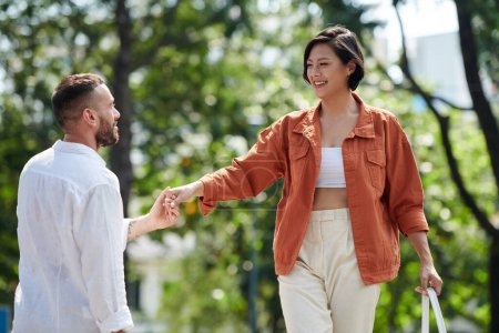 Photo for Smiling woman in orange denim jacket holding hand of boyfriend when walking and balancing on curb - Royalty Free Image