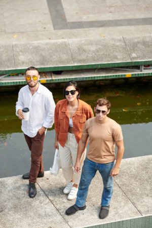 Téléchargez les photos : Groupe d'amis en lunettes de soleil debout sur l'embarquement de la rivière et regardant la caméra - en image libre de droit
