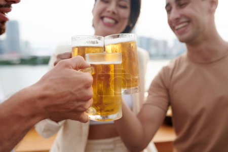 Photo for Close-up image of young people clinking mugs with cold beer at brewery bar - Royalty Free Image