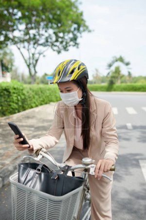 Foto de Joven empresaria en máscara médica comprobando teléfono inteligente en camino a la oficina - Imagen libre de derechos