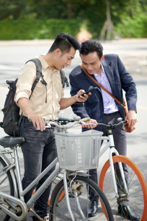 Téléchargez les photos : Jeune homme d'affaires asiatique montrant une nouvelle application mobile ou une vidéo intéressante sur smartphone à un collègue - en image libre de droit