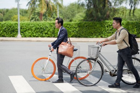 Photo for Determined Vietnamese businesssmen with bicycles crossing road in city when coming to work in morning - Royalty Free Image
