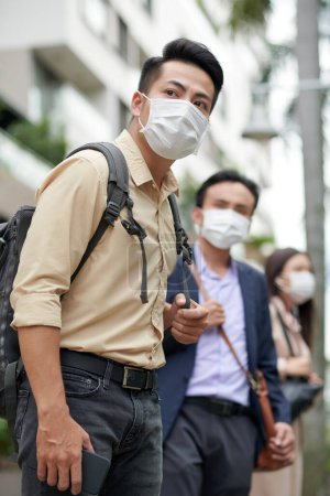 Photo for Hurrying anxious young Asian man in protective mask waiting for taxi or bus - Royalty Free Image