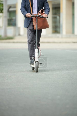 Téléchargez les photos : Homme d'affaires, enseignant ou homme politique avec sac en faux cuir chevauchant sur scooter électrique au bureau - en image libre de droit