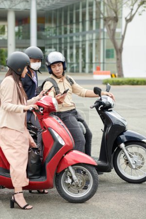 Téléchargez les photos : Collègues d'affaires sur scooters discuter où aller pour la pause déjeuner et vérifier la disponibilité sur l'application smartphone - en image libre de droit