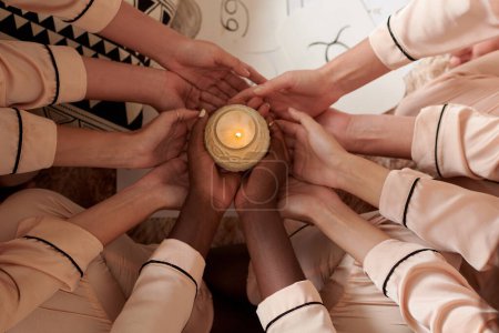 Foto de Amigos femeninos sosteniendo vela ardiente perfumada al realizar un ritual de fortura en casa - Imagen libre de derechos