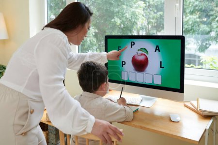 Téléchargez les photos : Professeur à domicile expliquant petit garçon comment résoudre le puzzle sur l'écran d'ordinateur - en image libre de droit