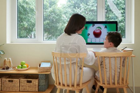 Photo for Home tutor teaching boy English language while they are sitting at computer desk - Royalty Free Image