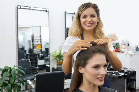 Téléchargez les photos : Coiffeur divisant les cheveux du client en sections pour appliquer de la teinture sur chacun - en image libre de droit
