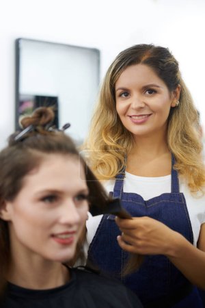 Photo for Smiling female hairdresser styling hair of young woman - Royalty Free Image