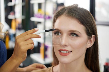 Photo for Make-up artist filling brows of young woman with brown pencil - Royalty Free Image