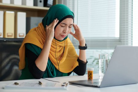 Téléchargez les photos : Développeur de logiciels musulmans souffrant de maux de tête sévères après avoir travaillé sur le projet toute la journée - en image libre de droit