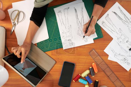 Téléchargez les photos : Mains de tailleur dessin croquis de mode à son dek, vue d'en haut - en image libre de droit