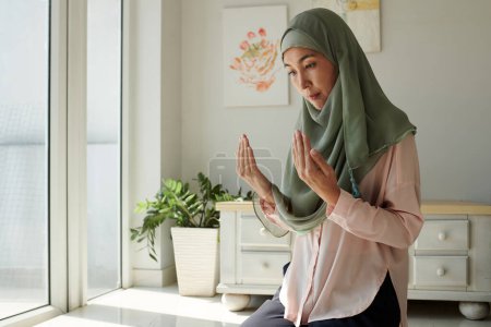 Foto de Mujer musulmana concentrada seria rezando en casa - Imagen libre de derechos