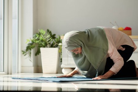 Foto de Mujer musulmana rezando sobre una alfombra pequeña en casa - Imagen libre de derechos