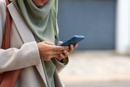 Photo for Cropped image of muslim woman answering text messages on smartphone - Royalty Free Image