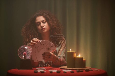 Photo for Portrait of serious sorcerer looking at tarot cards in her hands - Royalty Free Image