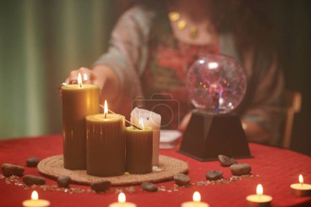 Téléchargez les photos : Image rapprochée de sorcier brûlant de grandes bougies de cire sur la table devant elle - en image libre de droit