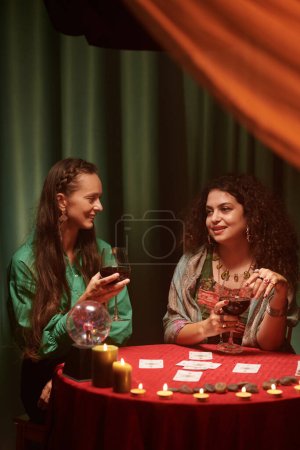 Photo for Smiling women drinking wine and discussing tarot cards spread - Royalty Free Image