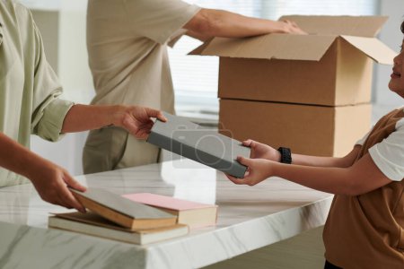 Photo for Hands of family packing books in cardboard boxes when moving out - Royalty Free Image