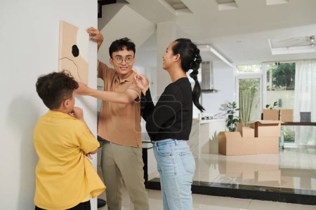 Téléchargez les photos : Joyeux tableau de famille accroché au mur dans leur nouvel appartement - en image libre de droit
