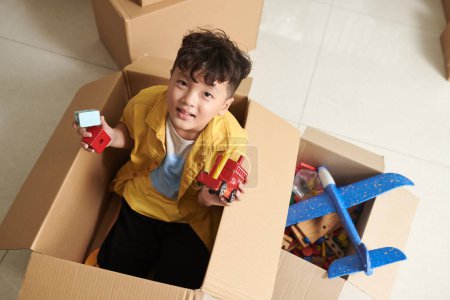 Foto de Niño preadolescente sentado en una caja de cartón y jugando con juguetes, vista desde arriba - Imagen libre de derechos