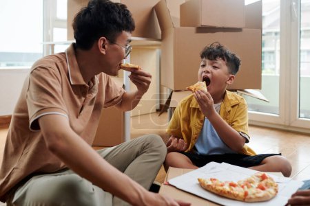 Photo for Hungry father and son eating pizza in their new apartment - Royalty Free Image