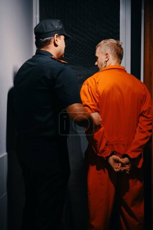 Foto de Oficial de la cárcel caminando criminal en uniforme naranja a la sala - Imagen libre de derechos