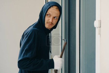 Photo for Burglar with crowbar breaking door and looking away - Royalty Free Image