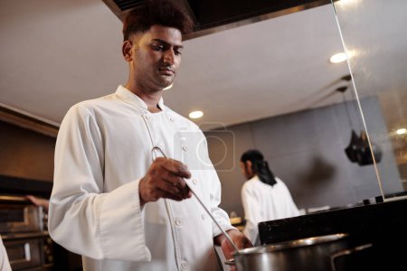 Foto de Chef serio en uniforme blanco mezclando sopa en una cacerola grande - Imagen libre de derechos
