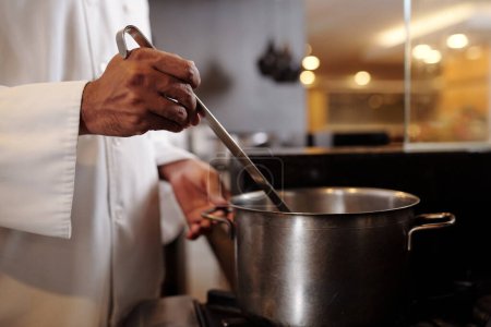 Photo for Cropped image of cook putting soup from big saucepan in plates - Royalty Free Image