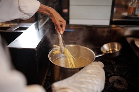 Foto de Manos de cocinero usando pinzas de cocina al sacar espaguetis de la cacerola - Imagen libre de derechos