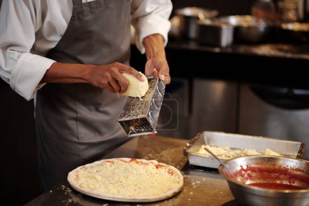 Foto de Fabricante de pizza trituración de queso mozzarella sobre pizza - Imagen libre de derechos