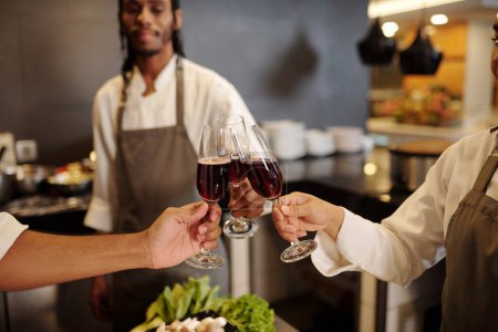 Téléchargez les photos : Image rapprochée de cuisiniers cliquetis verres de vin rouge après avoir terminé le travail dans le restaurant - en image libre de droit