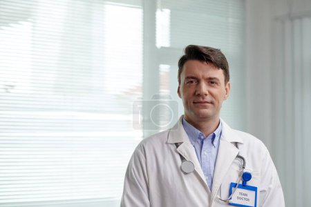 Téléchargez les photos : Portrait d'un chirurgien plastique souriant et confiant en blouse blanche debout dans un cabinet médical - en image libre de droit